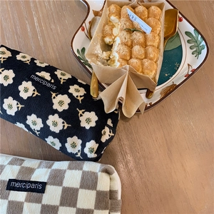 Detail of floral and checkerboard corduroy bags with merciparis label on a wooden desk