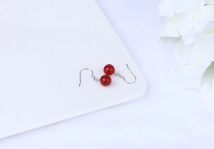 Detailed close-up of red agate bead drop earrings on a white ceramic display tray