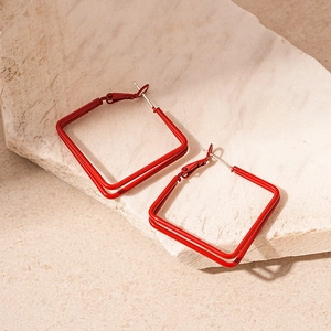 Detail of red square C-shaped geometric earrings with smooth painted finish