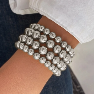 Macro detail of four stacked silver ball chain bracelets on a model's wrist with denim