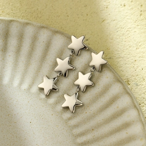 Macro detail of silver triple star drop earrings on a minimalist textured ceramic plate