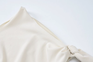 Detail of cream off-white summer dress featuring elegant shoulder knot and smooth knit texture