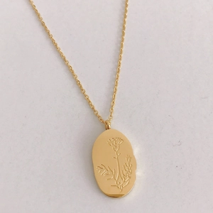 Detail of gold oval pendant with engraved flower pattern and irregular edges
