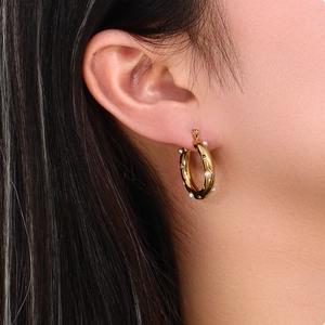 Close-up of gold stainless steel hoop earrings with white pearls on a model's ear