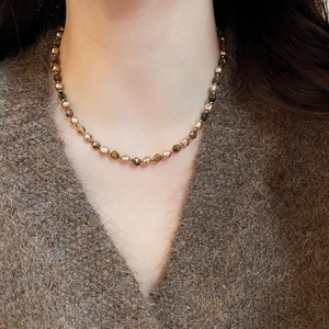 Detail of beaded necklace with tiger eye stones and gold beads on a brown sweater
