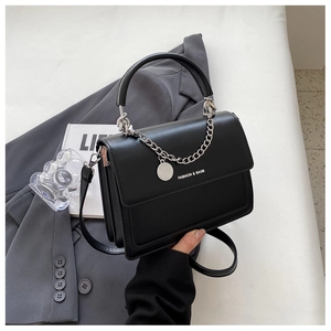 Detail of a black square flap handbag with glossy finish and silver chain decoration
