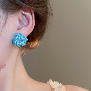 Detailaufnahme eines blauen Kristall-Ohrsteckers in Blumenform am Ohr des Models