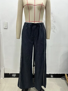 Détail d'un pantalon large en denim foncé avec bandes latérales blanches et cordon