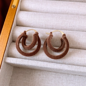 Detail of brown velvet double hoop earrings with golden hooks in a soft jewelry tray