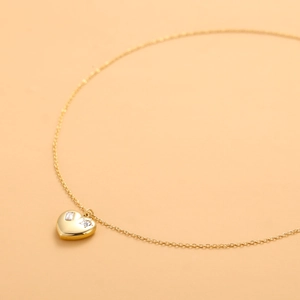 Minimalist gold heart pendant necklace with sparkling crystal inlay on warm background