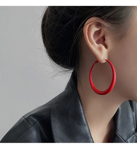 Side view of large red matte hoop earrings worn by a model in a black leather jacket
