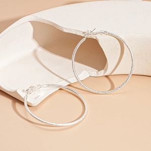 Detailed close-up of silver hoop earrings with textured finish on ceramic display