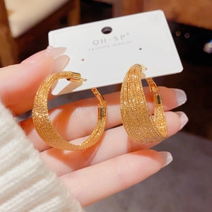Detailed macro shot of champagne gold hoop earrings with intricate woven metal texture