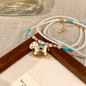 Close-up of pearl necklace with white enamel rocking horse pendant and colorful beads