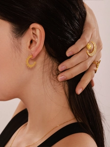 Detail view of gold sunburst earrings and star ring with 18K PVD finish on model