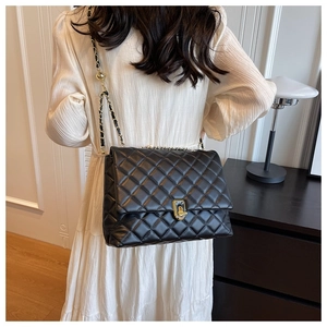 Classic black quilted shoulder bag with gold chain strap shown on a white dress