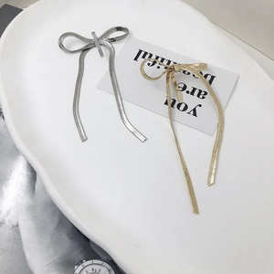 Minimalist metal bow earrings in gold and silver finish on a decorative tray