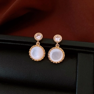 Detail of vintage gold earrings with round zircon studs and white resin shell pendants