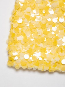 Détail d'une robe courte jaune vif avec de grandes paillettes rondes superposées