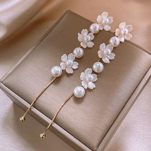 Detailed view of elegant gold chain earrings with pearls and white shell flowers