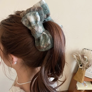 Detailed view of a large velvet bow hair clip worn on a low ponytail in a warm indoor setting