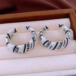Close-up of C-shaped earrings with black and white ribbon wrap and letter print