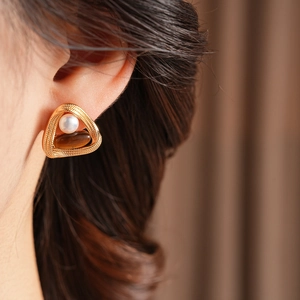 Detail of vintage tiger eye and pearl earrings on model with gold triangular frame