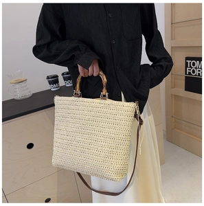 Detail of woven straw tote bag featuring bamboo handles and a brown leather strap