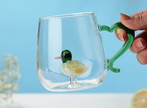 Close-up of a clear glass mug featuring a green handle and an internal duck figurine