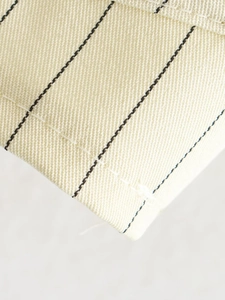 Macro view of creamy white fabric texture with thin black stripes and detailed stitching
