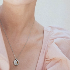 Hammered circular silver necklace featuring a rectangular orange zircon pendant on model