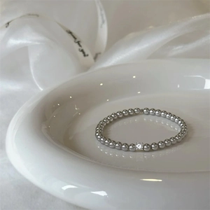 Elegant pearl and zircon beaded bracelet displayed on a white porcelain dish with silk ribbons