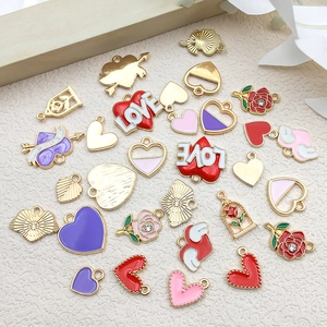 Flat lay of assorted gold enamel heart pendants with rose and wing charms for DIY jewelry