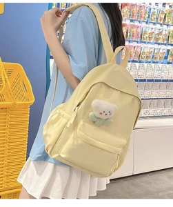 Side view of a bright yellow casual backpack featuring a cute white teddy bear plush charm