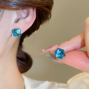 Détail d'un clou d'oreille en cristal bleu ciel à coupe carrée porté sur l'oreille