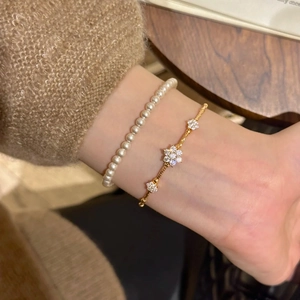 Detail of elegant gold flower charm bracelet and white pearl bracelet on a woman's wrist