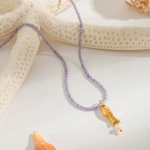Detail of beaded necklace with purple beads, gold fish pendant, and white pearl accent