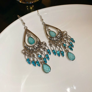 Macro detail of silver teardrop tassel earring with turquoise stone on white plate