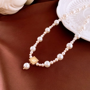 Close-up of pearl necklace with gold rectangle pendant on dark silk background