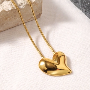 Detail of 18k gold heart pendant on a polished snake chain against a textured background