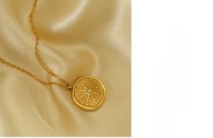 Macro detail of gold stainless steel starburst coin pendant on luxury silk fabric