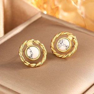 Detailed macro of gold twisted metal earrings with marble stones on jewelry box