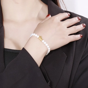 Detailed view of beaded shell pearl bracelet with gold pig charm on a model's wrist