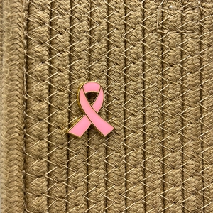 Detail of pink enamel ribbon brooch with gold metal edges on a textured woven background