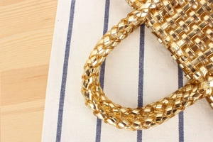 Détail de la texture tressée dorée et de la poignée cylindrique du sac à main chic