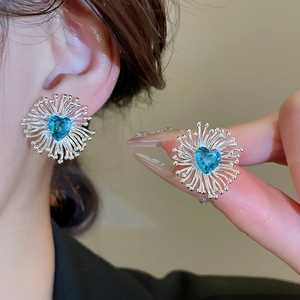 Gros plan de boucles d'oreilles cœur en zircon bleu avec pétales en argent sur l'oreille