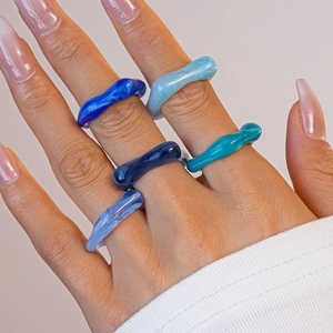 Gros plan de cinq bagues en acrylique bleu marbré sur les doigts avec détails en résine