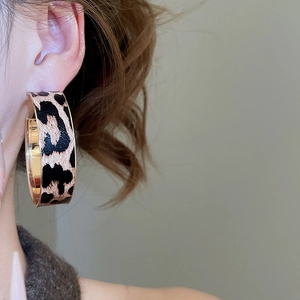 Macro view of gold-rimmed leopard print C-shape earrings worn on the earlobe