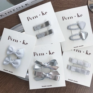 Close-up of silver bow and heart leather hair clips on display card with wooden background