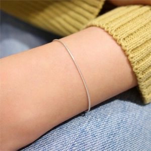 Close-up of a minimalist silver snake chain bracelet on a woman's wrist in a casual setting